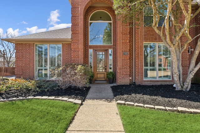 entrance to property featuring brick siding and a shingled roof