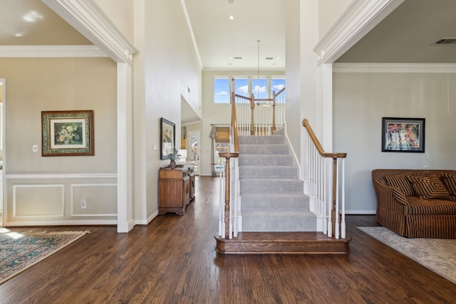 stairs with wood finished floors, visible vents, baseboards, a towering ceiling, and crown molding