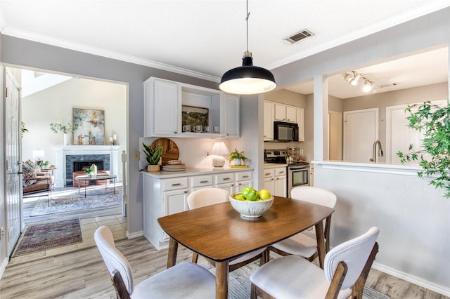 dining space featuring visible vents, a fireplace, light wood-style floors, and ornamental molding