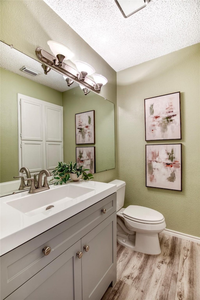 bathroom with vanity, wood finished floors, visible vents, a textured ceiling, and toilet