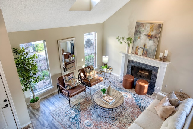 living room with a tiled fireplace, vaulted ceiling, wood finished floors, and a textured ceiling