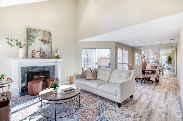 living area featuring visible vents, baseboards, light wood finished floors, a high ceiling, and a tiled fireplace