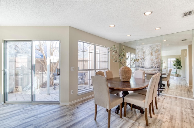 dining space featuring visible vents, light wood finished floors, and a textured ceiling