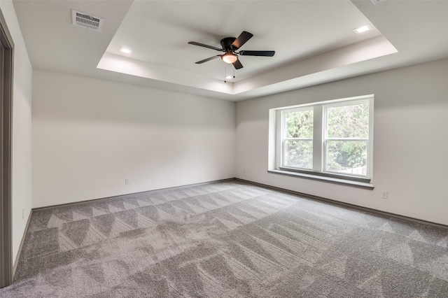 spare room with visible vents, ceiling fan, baseboards, a tray ceiling, and carpet floors