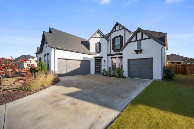 tudor home featuring fence, concrete driveway, a front yard, stucco siding, and a garage