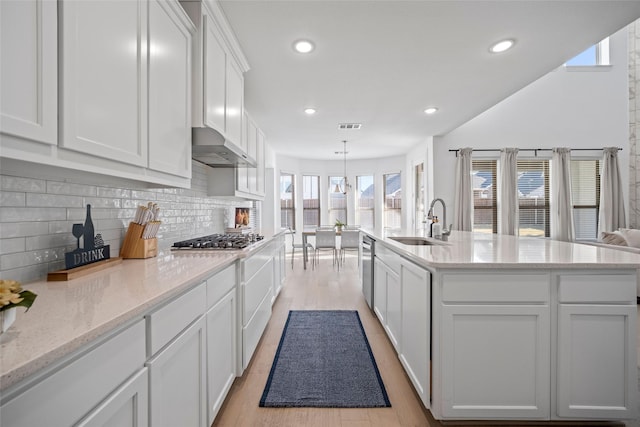 kitchen with visible vents, stainless steel appliances, a sink, white cabinetry, and wall chimney range hood