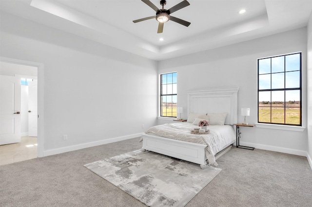 carpeted bedroom with a tray ceiling, multiple windows, and baseboards