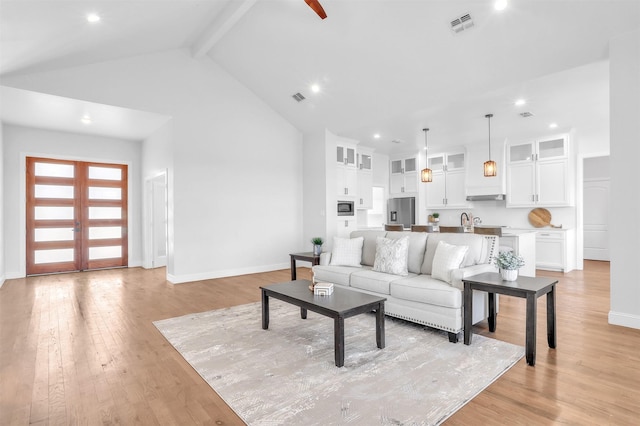 living area featuring visible vents, baseboards, light wood-style floors, and high vaulted ceiling