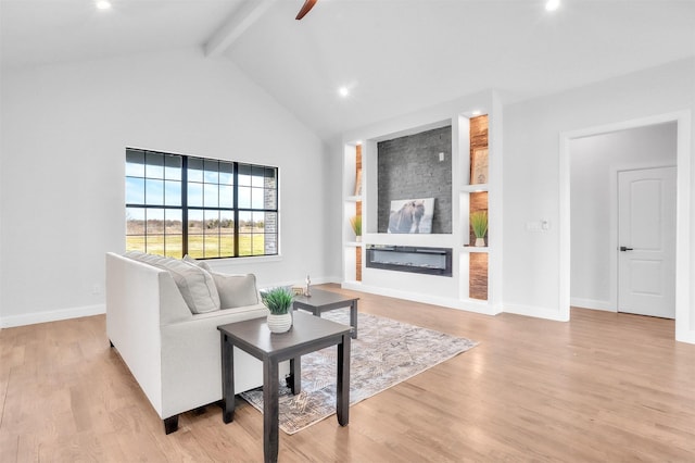 living area featuring a glass covered fireplace, beam ceiling, baseboards, and light wood finished floors