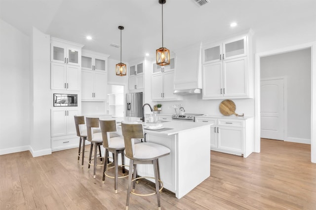 kitchen with premium range hood, a kitchen bar, light countertops, stainless steel appliances, and a kitchen island with sink