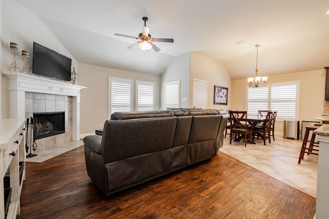 living area with visible vents, a tile fireplace, ceiling fan with notable chandelier, wood finished floors, and vaulted ceiling