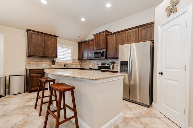 kitchen with backsplash, a kitchen island, light stone countertops, dark brown cabinetry, and stainless steel appliances