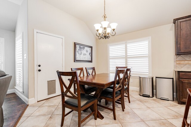 dining space with light tile patterned floors, baseboards, lofted ceiling, and an inviting chandelier