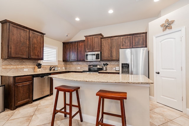 kitchen featuring dark brown cabinets, a center island, a breakfast bar area, vaulted ceiling, and stainless steel appliances