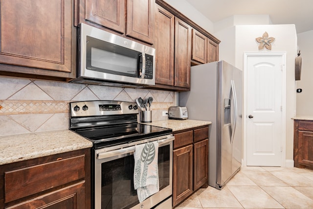 kitchen featuring tasteful backsplash, light stone countertops, stainless steel appliances, and light tile patterned flooring