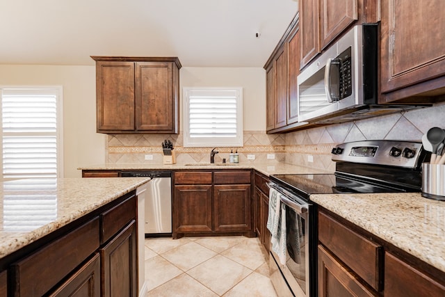 kitchen featuring a sink, light stone counters, tasteful backsplash, appliances with stainless steel finishes, and light tile patterned floors