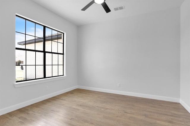 empty room featuring a ceiling fan, light wood-style flooring, baseboards, and visible vents