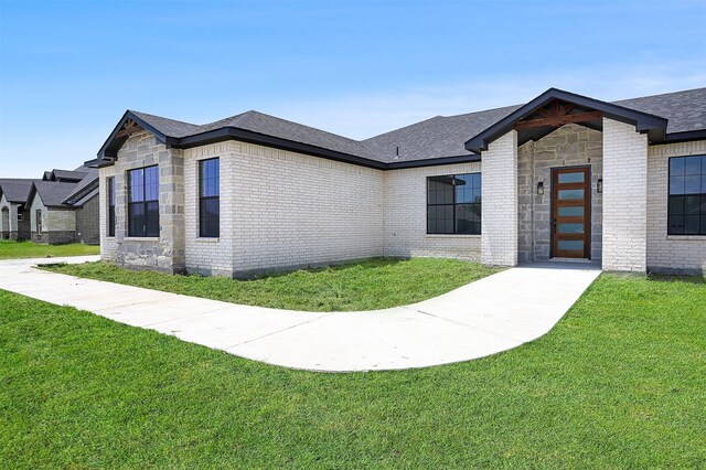 view of front facade with stone siding, brick siding, a front yard, and a shingled roof