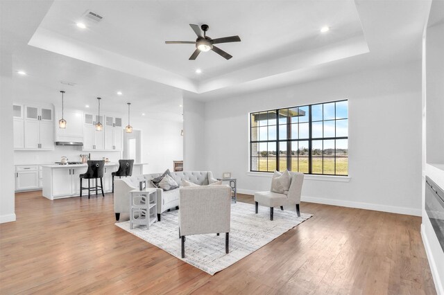 living area with light wood finished floors, recessed lighting, baseboards, and a tray ceiling