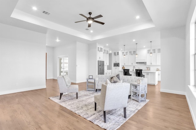 living area with light wood-type flooring, a tray ceiling, baseboards, and visible vents