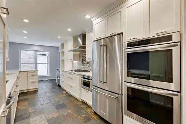 kitchen featuring white cabinetry, stainless steel appliances, wall chimney exhaust hood, and light countertops