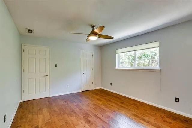 unfurnished bedroom with visible vents, baseboards, wood finished floors, and a ceiling fan