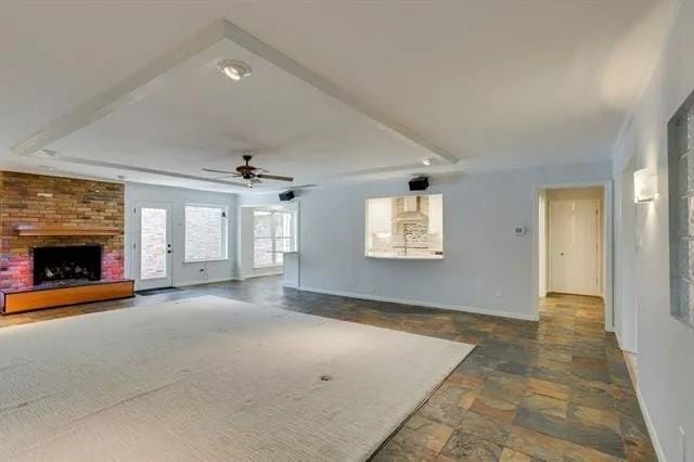 unfurnished living room featuring a tray ceiling, baseboards, a brick fireplace, and stone finish flooring