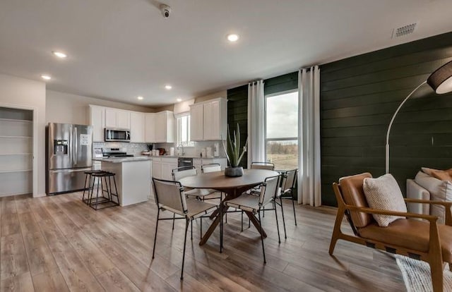 dining area featuring wooden walls, recessed lighting, and light wood-style floors