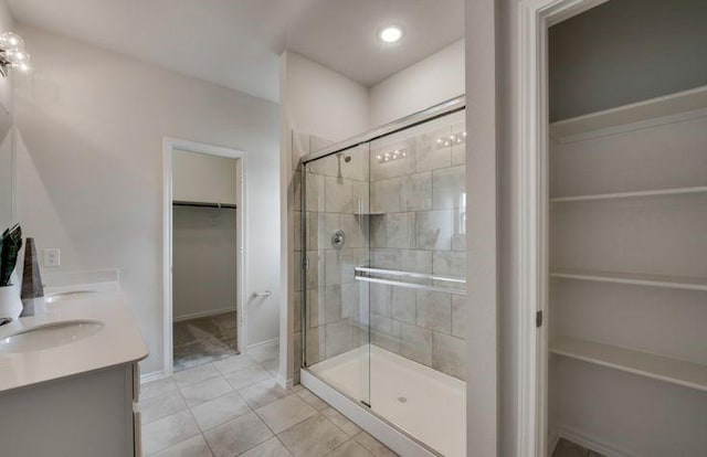 full bathroom featuring a shower stall, a walk in closet, baseboards, tile patterned floors, and a sink