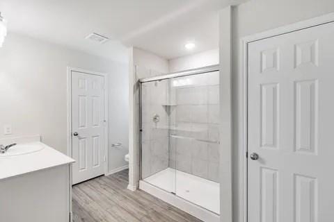 bathroom featuring visible vents, toilet, a stall shower, wood finished floors, and vanity