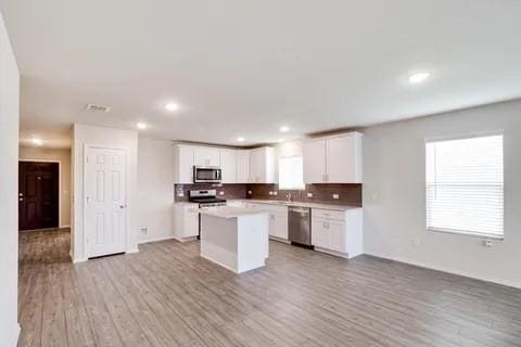 kitchen featuring appliances with stainless steel finishes, white cabinets, a center island, and light wood finished floors