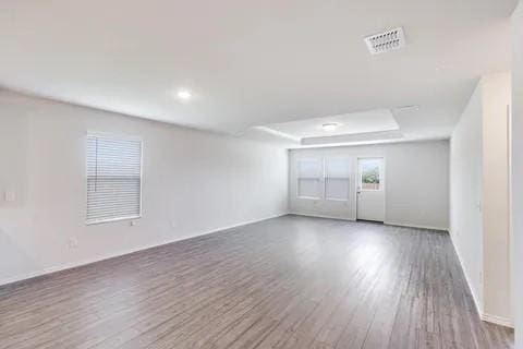 empty room featuring a tray ceiling, visible vents, and wood finished floors