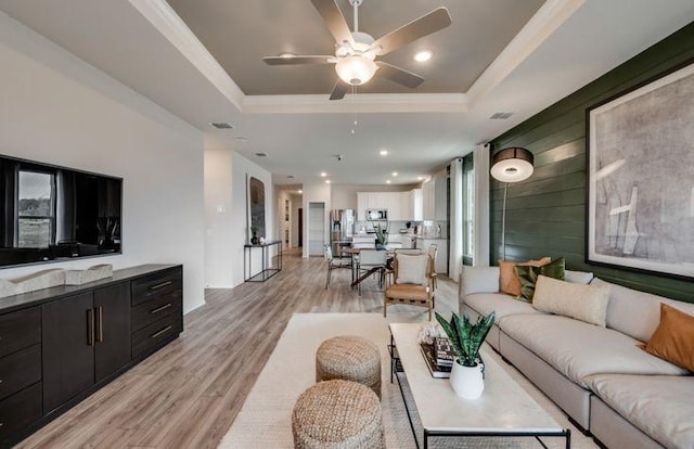 living area with visible vents, light wood finished floors, ceiling fan, crown molding, and a raised ceiling