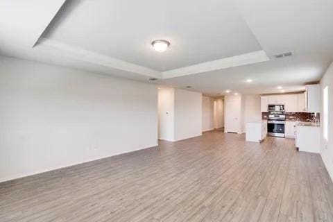 unfurnished living room featuring a raised ceiling, visible vents, and light wood finished floors