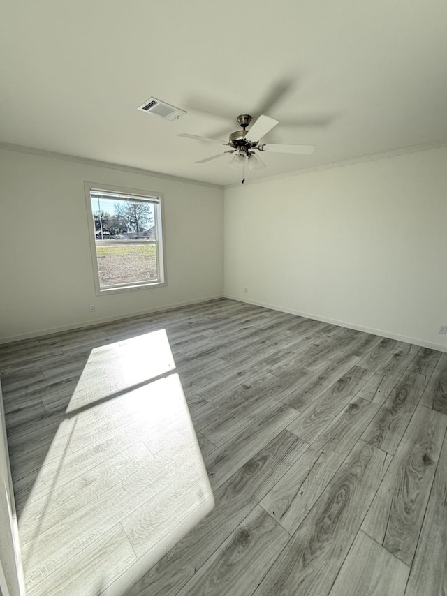 spare room with ceiling fan, visible vents, baseboards, and wood finished floors