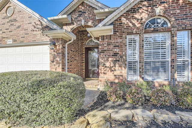 doorway to property featuring an attached garage and brick siding