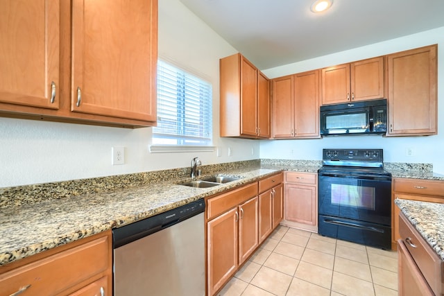 kitchen with light tile patterned floors, brown cabinetry, light stone countertops, a sink, and black appliances