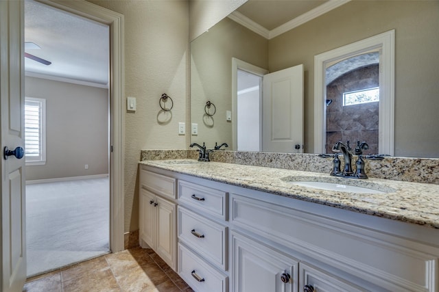 bathroom featuring crown molding, baseboards, double vanity, a tile shower, and a sink