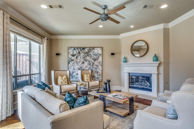 living area featuring baseboards, visible vents, ceiling fan, ornamental molding, and a glass covered fireplace