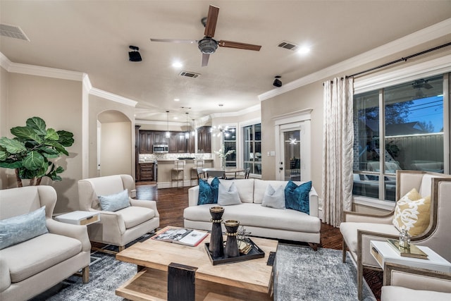 living area featuring arched walkways, visible vents, dark wood finished floors, and crown molding