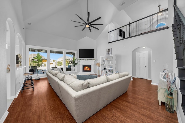 living room featuring visible vents, a ceiling fan, a warm lit fireplace, dark wood-style floors, and arched walkways