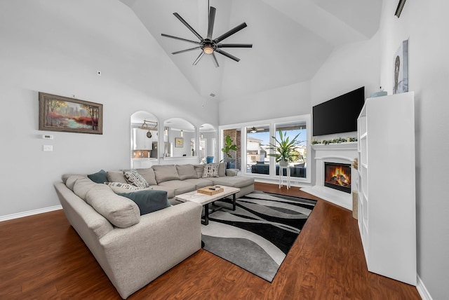 living area featuring a lit fireplace, high vaulted ceiling, a ceiling fan, and wood finished floors