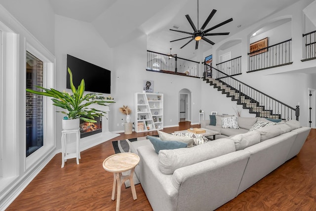 living room featuring ceiling fan, wood finished floors, arched walkways, a towering ceiling, and stairs