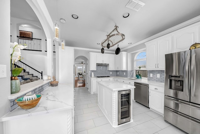 kitchen with stainless steel appliances, arched walkways, beverage cooler, and white cabinetry