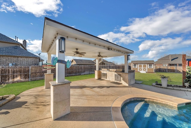 view of swimming pool featuring a yard, a fenced backyard, an outdoor structure, a ceiling fan, and a patio