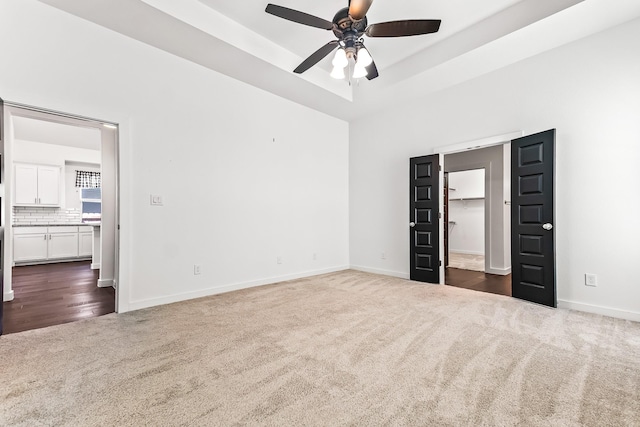 unfurnished bedroom featuring a tray ceiling, baseboards, a walk in closet, and dark carpet