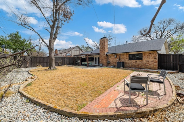 back of property with a patio area, brick siding, a fenced backyard, and a chimney