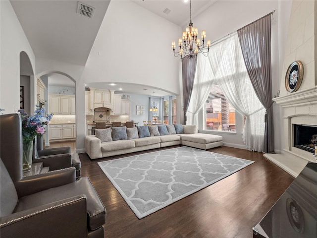 living room with visible vents, dark wood-type flooring, high vaulted ceiling, a large fireplace, and an inviting chandelier