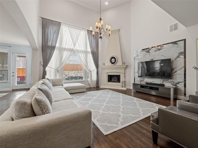 living room featuring visible vents, a fireplace with raised hearth, wood finished floors, an inviting chandelier, and a towering ceiling