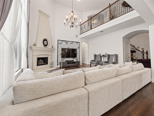 living area with dark wood finished floors, a high ceiling, a fireplace with raised hearth, arched walkways, and stairs